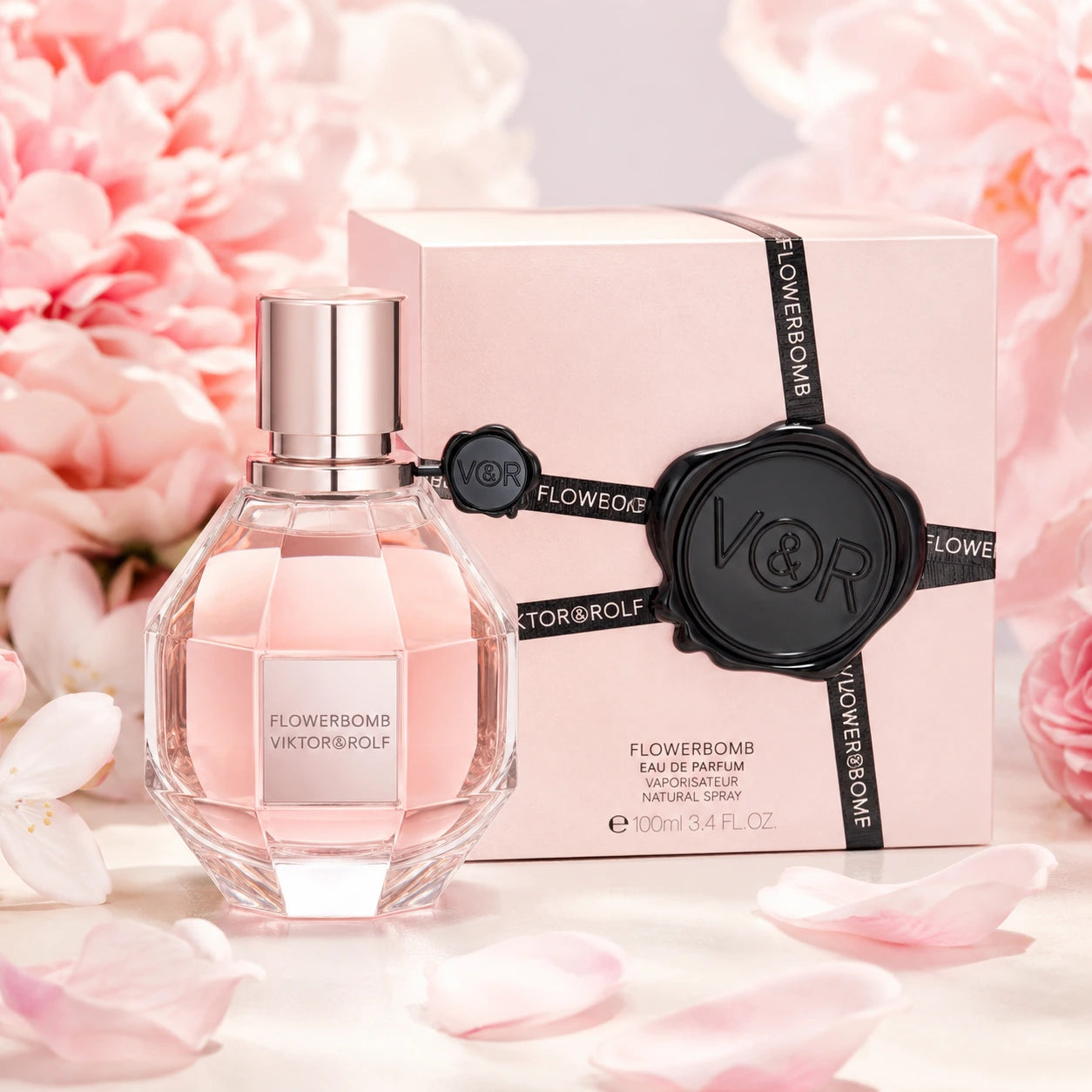 Viktor & Rolf Flowerbomb 100ml EDP women's perfume hero image with the faceted pink bottle and pink gift-style box styled with soft peony blooms and scattered petals.