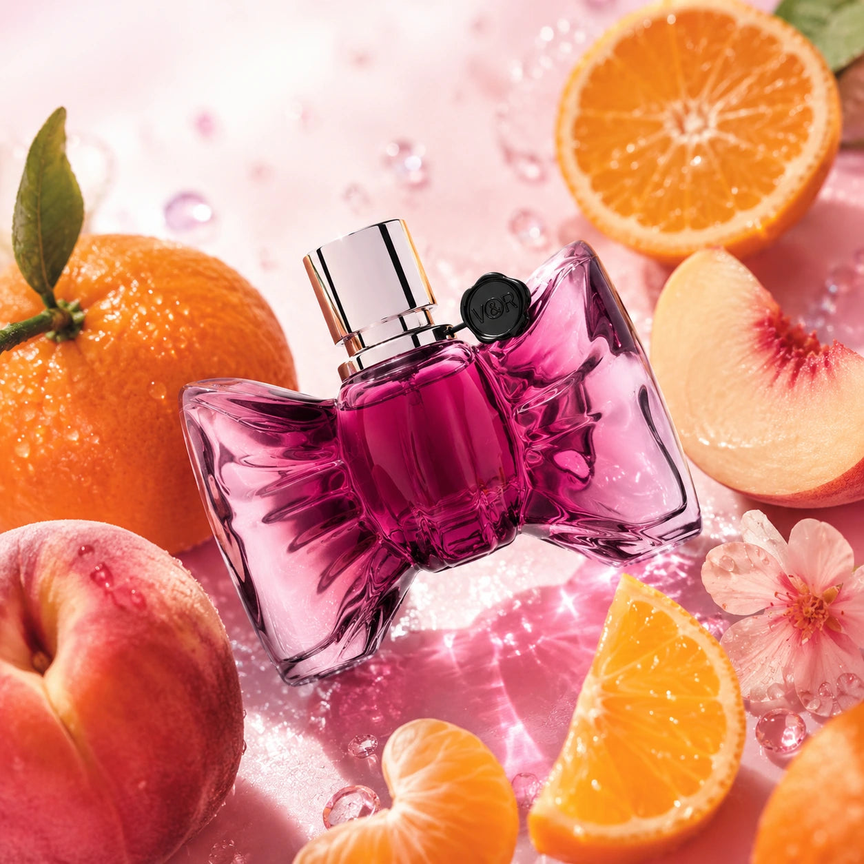 Viktor & Rolf Bonbon EDP 90ml top notes image with mandarin, orange and peach surrounding the original Bonbon perfume bottle in a sparkling fruity pink setting.