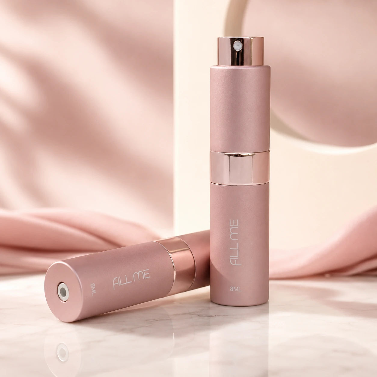 Fill Me refillable 8ml travel perfume atomiser bottle pink hero image showing two pink matte atomisers in a soft luxury blush setting.