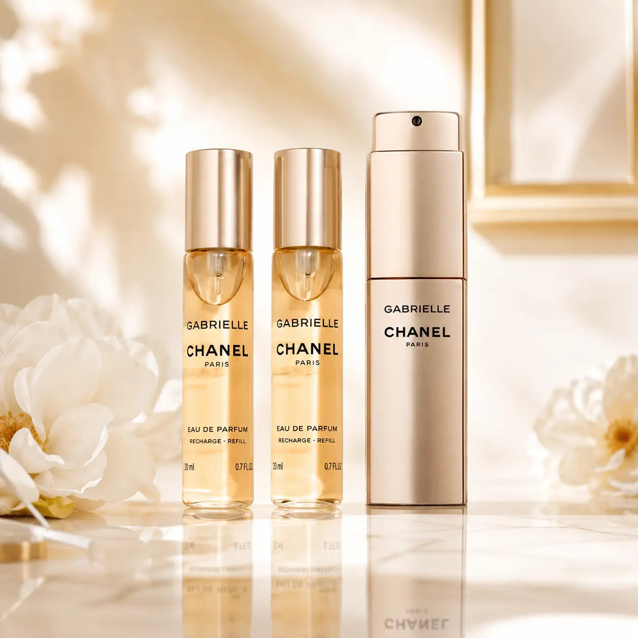 Chanel Gabrielle perfume bottles on a reflective surface with floral background
