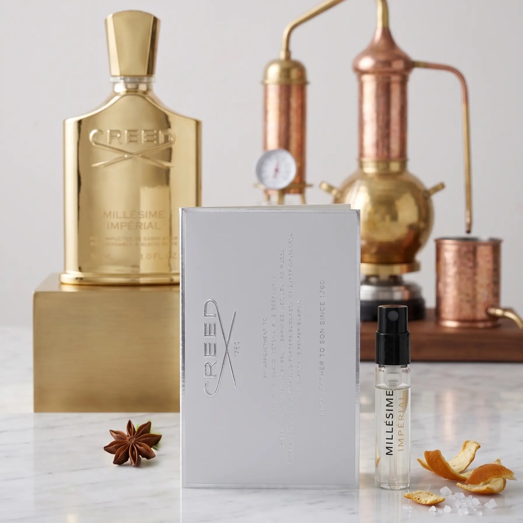 Creed perfume vial and packaging on a marble surface with a copper still in the background.