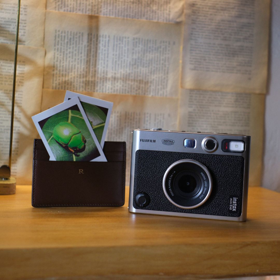 Fujifilm Instax mini evo instant Film camera with instant photos and a wallet on a wooden surface