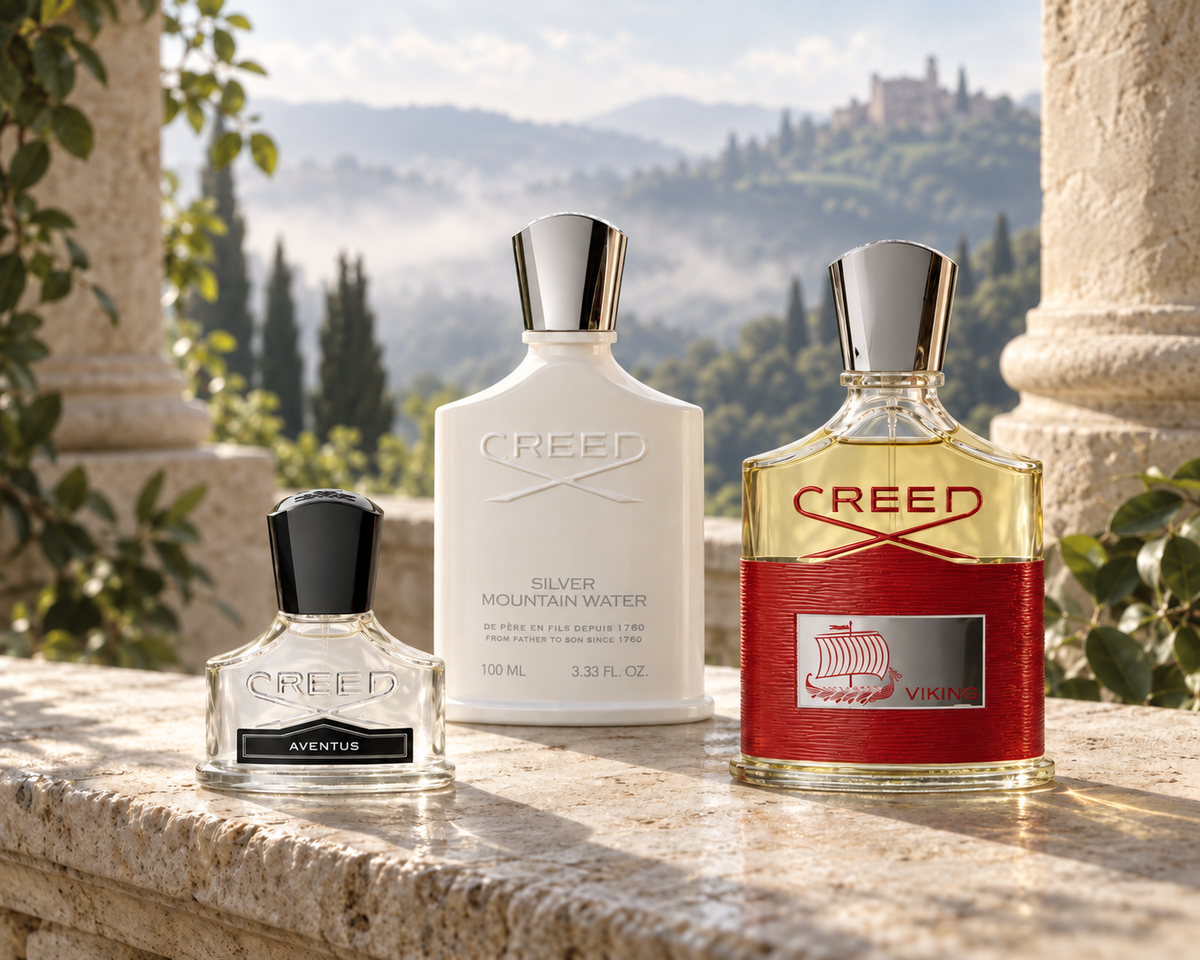 Creed Aventus, Silver Mountain Water and Viking bottles on pale stone overlooking misty green hills.